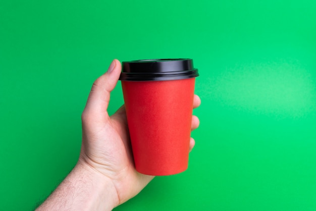 Una mano che tiene un rosso porta via la tazza su verde