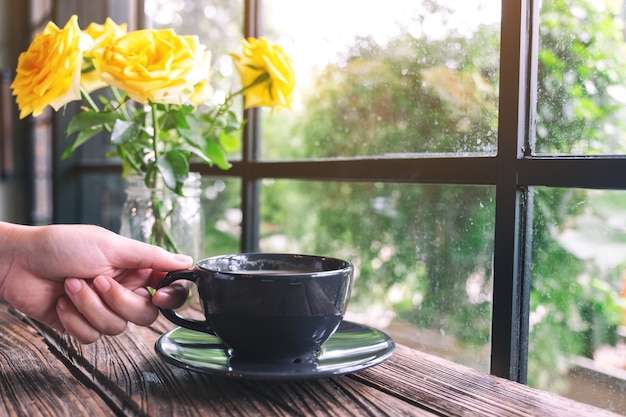 una mano che tiene una tazza di caffè caldo sul tavolo di legno