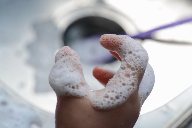 Una mano con una bolla di sapone mentre si lava le mani con fondo lavello in acciaio