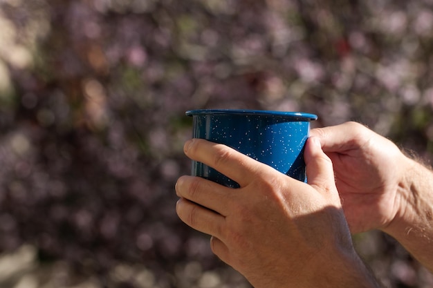 Una mano d'uomo che tiene una tazza di caffè blu con la natura sullo sfondo