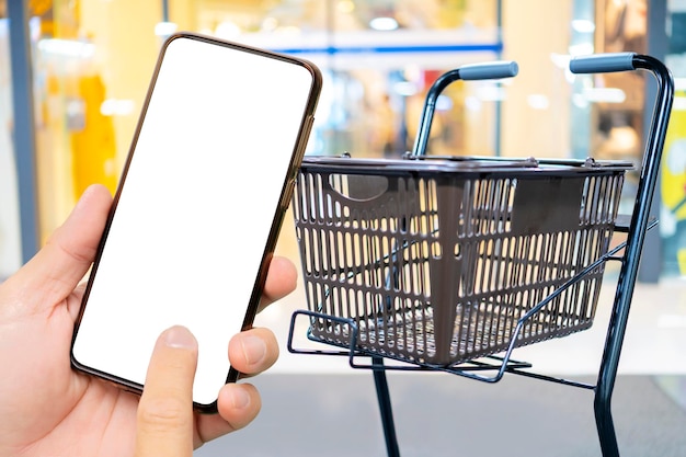 Una mano d'uomo che tiene uno smartphone nero Smartphone touch screen in una mano Carrello parcheggiato davanti all'ingresso del supermercato concetto di shopping online