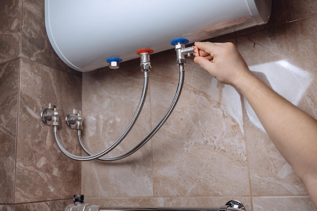 Una mano d'uomo regola lo scaldabagno a parete del bagno Gira i rubinetti Piastrelle in marmo beige