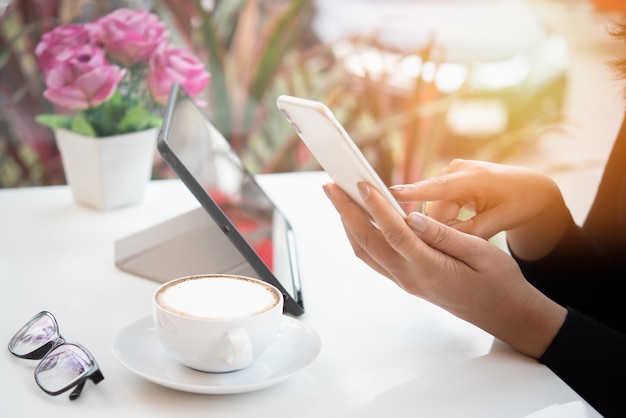 Una mano della donna che utilizza smartphone vicino ad una finestra nella caffetteria