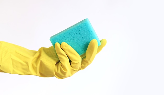 Una mano di donna con un guanto di lattice giallo tiene una spugna per lavare i piatti e pulisce i locali