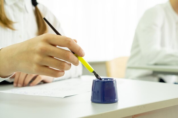 Una mano di donna con una penna stilografica e un calamaio su una scrivania luminosa in classe