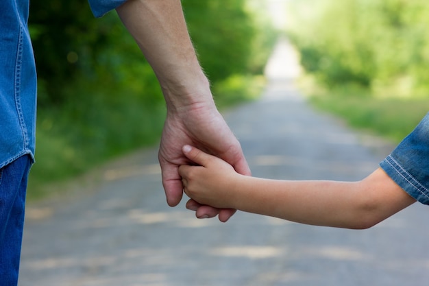 Una mano di genitore e bambino felici sulla natura sulla strada sullo sfondo del parco