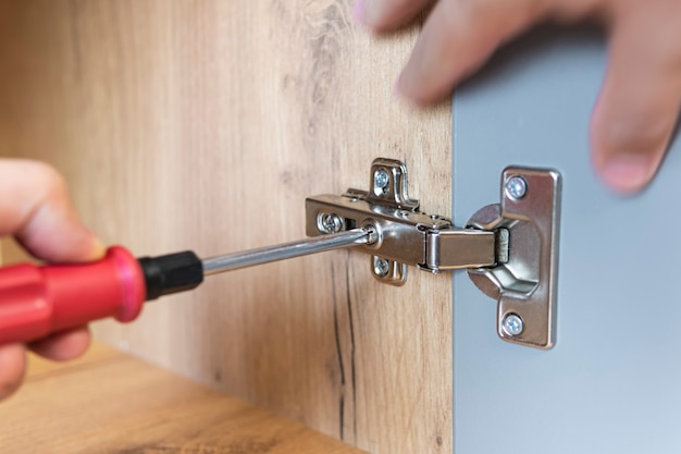 Una mano di un assemblatore di mobili che regola un meccanismo per aprire la porta del tavolo dell'ufficio con un cacciavite. Avvicinamento. Concetto di riparazione domestica. Autoassemblaggio di mobili.