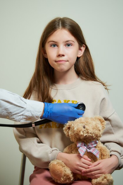 Una mano di un medico detiene uno stetoscopio che sente il battito cardiaco di una giovane paziente.