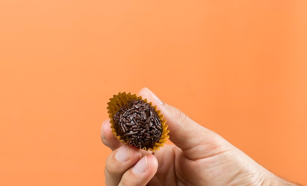 Una mano di una donna che tiene un brigadeiro vegano Tipico sfondo arancione dolce brasiliano