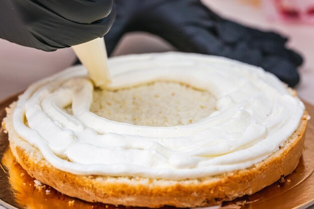 Una mano femminile con un guanto nero spremere la crema su una torta di formaggio con cocco