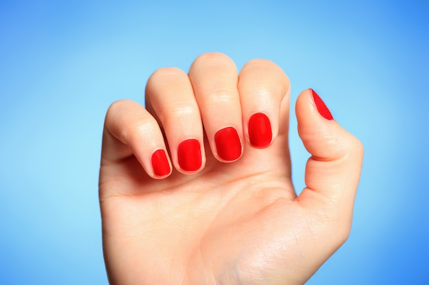 una mano femminile con unghie dipinte di rosso su sfondo blu