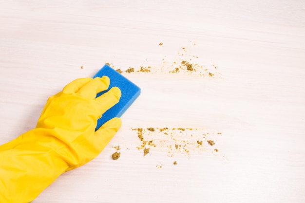 Una mano femminile in un guanto di gomma gialla salviettine con una spugna blu per lavare i piatti avanzi di cibo su un tavolo di legno