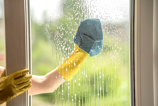 Una mano femminile in un guanto giallo lava una finestra sporca in estate. Straccio in mano. Pulizia dell'appartamento.