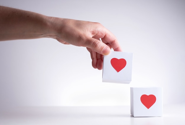 Una mano femminile porta una scatola bianca con un cuore rosso a un'altra scatola rossa con un cuore rosso, da vicino.