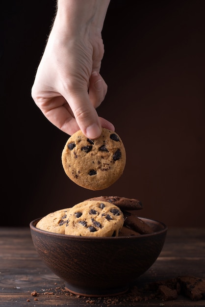 Una mano femminile prende un biscotto con gocce di cioccolato da un piatto su un tavolo di legno scuro