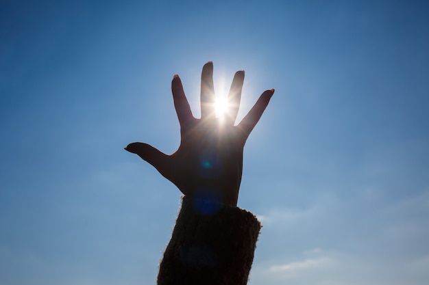 Una mano femminile si staglia contro un cielo azzurro e un sole splendente