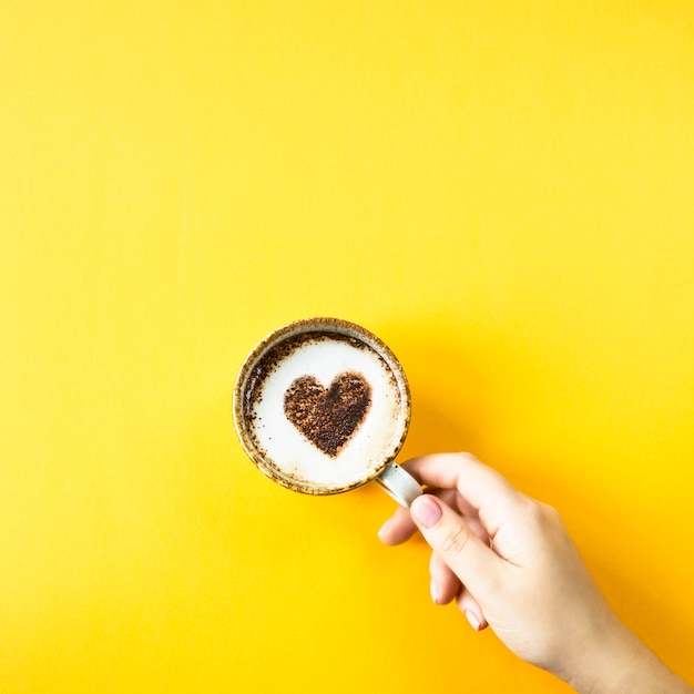 Una mano femminile tiene una tazza di caffè su cui è disegnato un cuore