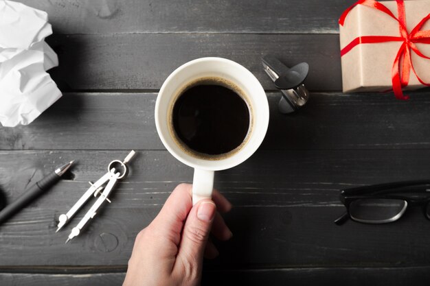 Una mano femminile tiene una tazza di caffè sul tavolo di legno