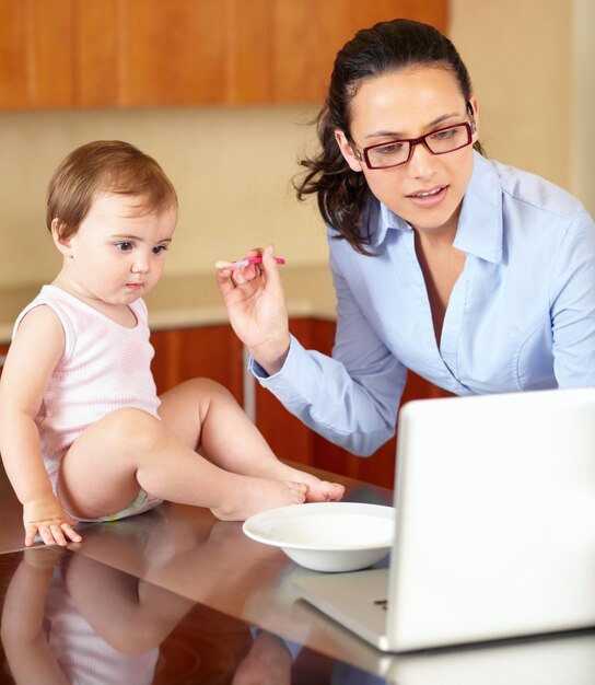 Una mano in più sarebbe utile Inquadratura di una mamma single che allatta il suo bambino mentre cerca di lavorare sul suo laptop