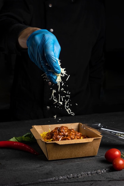 Una mano in un guanto blu che cosparge di formaggio grattugiato in un contenitore di peperoncino.