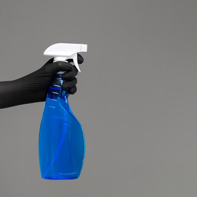 Una mano in un guanto di gomma tiene il detergente per vetri in un flacone spray