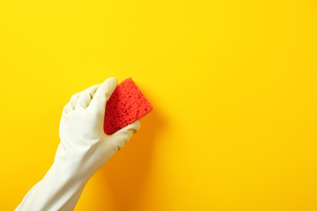 Una mano in un guanto di gomma verde tiene una spugna di lavaggio rossa su sfondo giallo