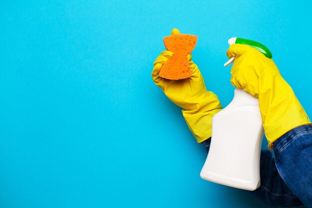 Una mano in un guanto giallo tiene uno spruzzo di liquido detergente su sfondo blu.