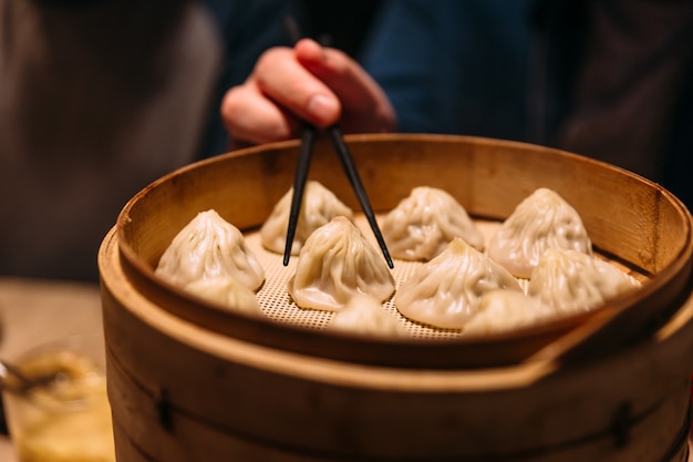 Una mano pizzica Xiao Long Bao (Soup Dumpling) con le bacchette di streamer di bambù.