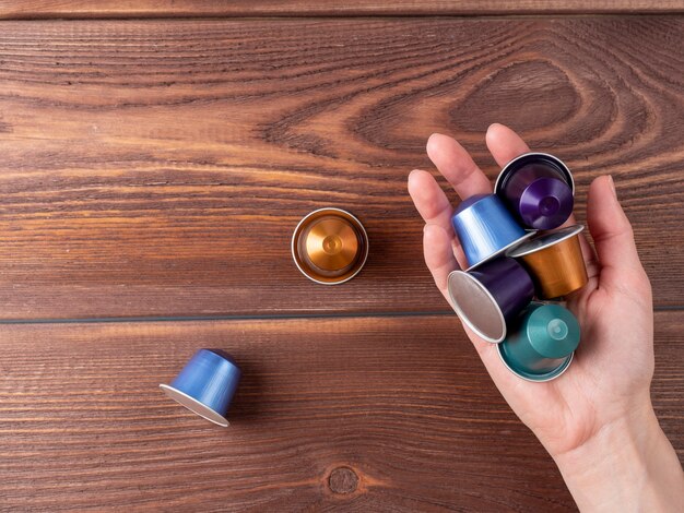Una mano tiene le capsule di caffè in alluminio colorato per la macchina da caffè su uno sfondo di legno marrone. Il concetto di soluzioni moderne per la conservazione e la preparazione del caffè