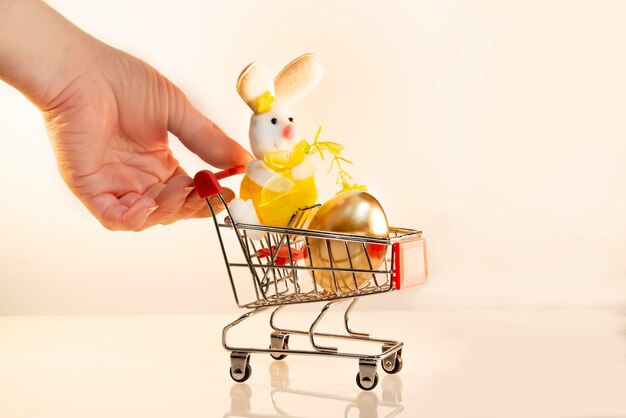 Una mano tiene un carrello con un uovo d'oro una lepre giocattolo un coniglietto di Pasqua vacanza Comprare souvenir