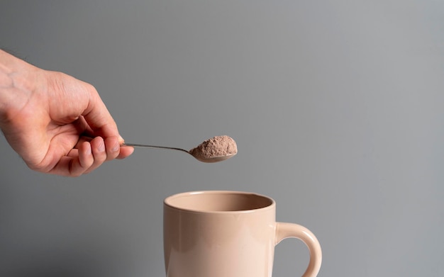 Una mano tiene un cucchiaio con la polvere di cacao e lo mette in una tazza con acqua calda