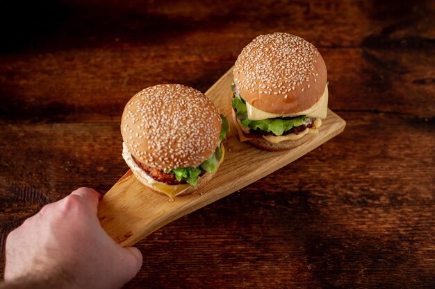 Una mano tiene una tavola di legno con due hamburger o hamburger Sfondo in legno scuro