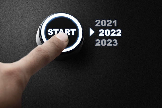 Una mano umana preme il pulsante di avvio per iniziare il 2022. Felice Anno Nuovo 2022