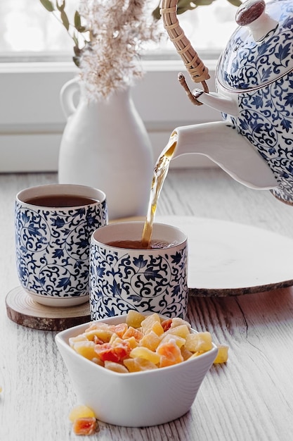 Una mano versa il tè da una teiera rami di cereali secchi per l'ora del tè in un vaso di ceramica bianca con un set da tè