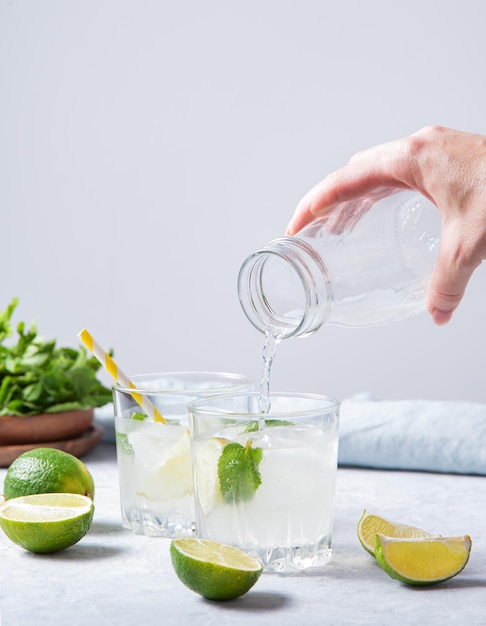 Una mano versa una limonata mojito al lime in un bicchiere sul tavolo con fette di lime e menta fresca Vista frontale e copia spazio immagine