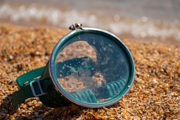 Una maschera da nuoto verde giace sulla sabbia.