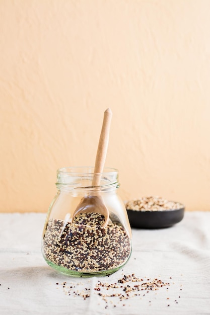 Una miscela di quinoa bianca rossa e nera cruda e un cucchiaio di legno in un barattolo su un panno Cibo sano senza glutine Vista verticale