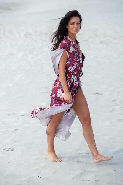 Una modella cammina sulla spiaggia indossando un abito floreale.