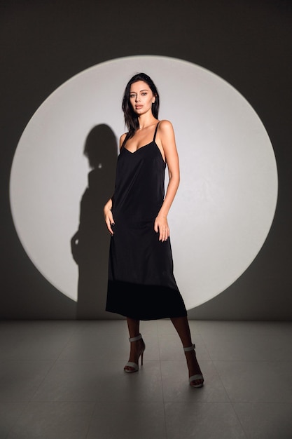Una modella con un abito nero si trova davanti a una luce rotonda.