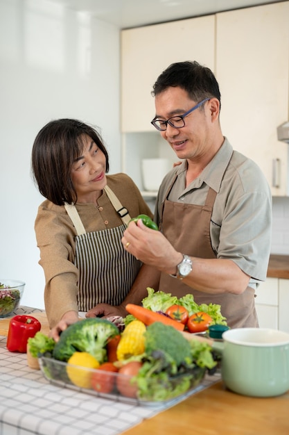 Una moglie e un marito asiatici adulti felici stanno cucinando insieme la loro sana colazione in cucina.