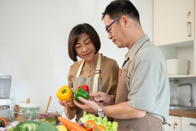 Una moglie e un marito asiatici adulti felici stanno cucinando insieme la loro sana colazione in cucina.