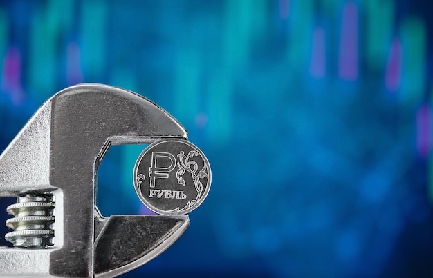 Una moneta con il simbolo del rublo russo su sfondo blu sfocato con un grafico di virgolette cadenti viene schiacciata con una chiave inglese Notizie sul default e il crollo dell'economia Testo libero