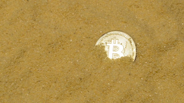 Una moneta cripto bitcoin su sabbia dorata brillante. trovare e minare criptovalute