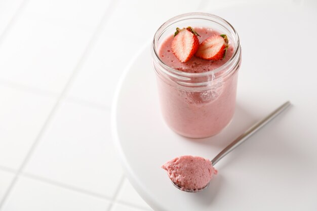 Una mousse di dessert alla fragola in vetro con cucchiaio su lavagna bianca su fondo di piastrelle bianche