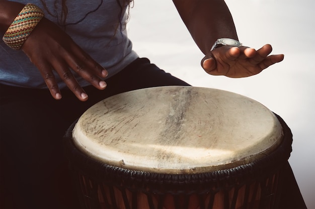 Una musicista africana suona il tamburo djembe. Lei è su uno sfondo bianco.