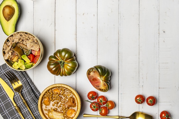 Una natura morta in insalata con pomodori dolci bonito in scatola uno stufato di lenticchie e posate d'oro