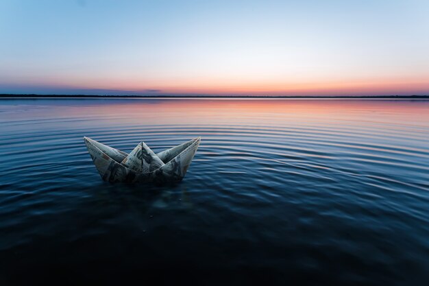 Una nave di carta fatta di banconote, fatta di dollari, galleggia nell'acqua sullo sfondo di un bellissimo tramonto. Origami da denaro, modello di business finanziario, copia spazio.