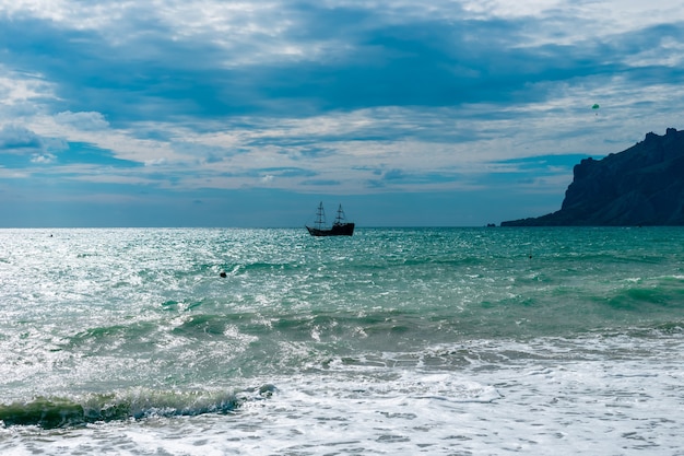 Una nave sta navigando sul mare sullo sfondo di un cielo nuvoloso scuro e montagne. Bellissimo paesaggio marino.