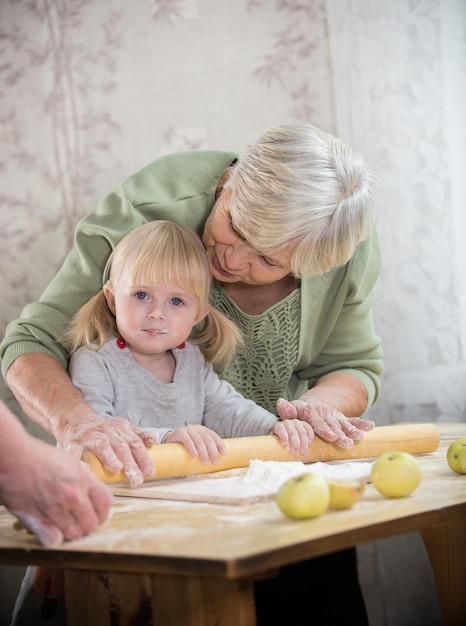 Una nonna che prepara le tortine con la nipote che arrotola la pasta