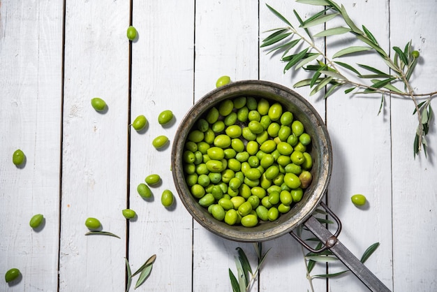 Una padella piena di olive verdi biologiche per preparare l'olio d'oliva su sfondo bianco
